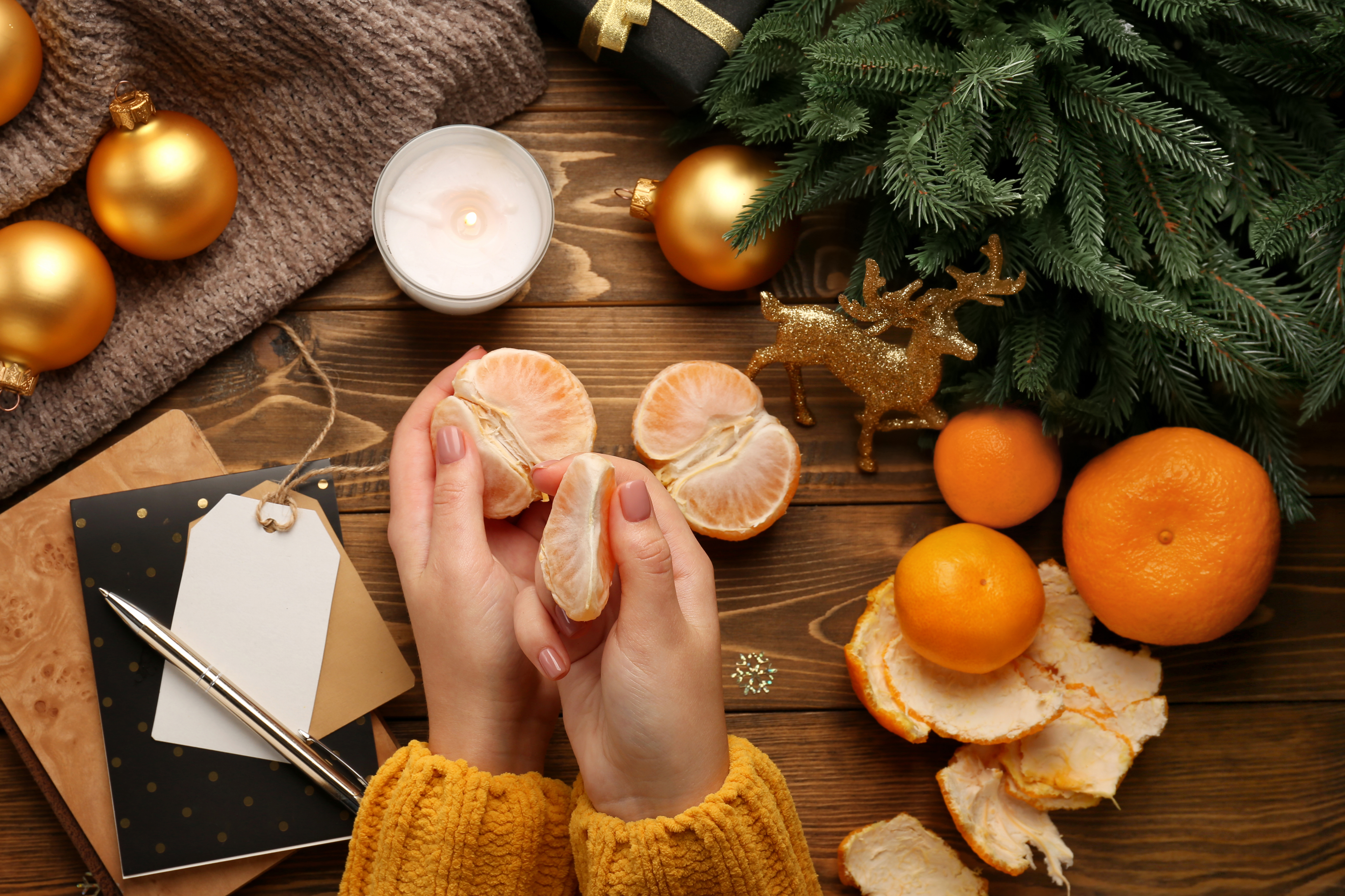 Två händer skalar en klementin bland julpynt på ett bord