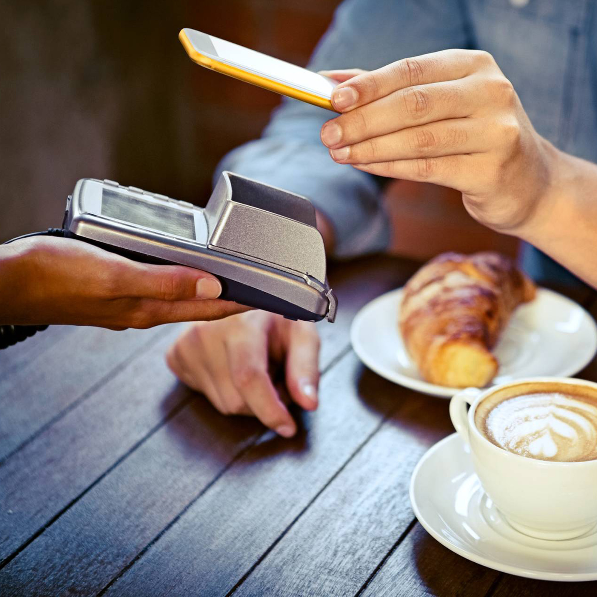 Person på ett café betalar med mobilen.